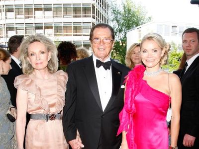 Christina Knudsen is wearing a pink dress, Roger Moore is wearing a tuxedo, and Kristina Tholstrup is wearing a peach color dress.